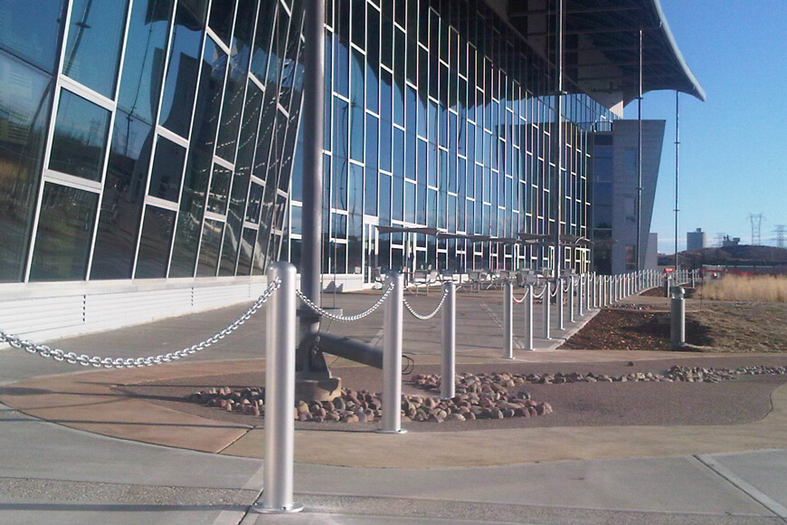 Varios bolardos de acero están unidos con una cadena en frente de un gran edificio moderno